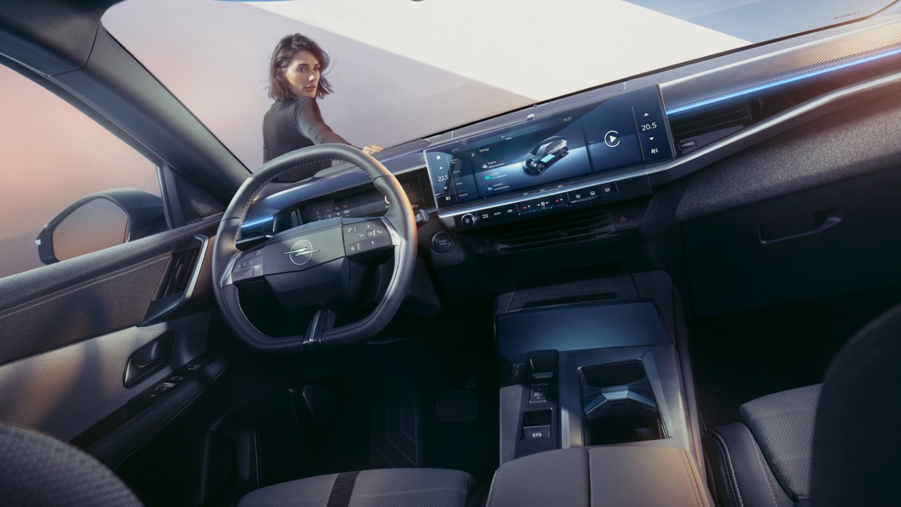Gros plan sur le système d'affichage Pure panel d'un nouvel Opel Grandland avec une femme s'appuyant sur une voiture et regardant à l'intérieur.