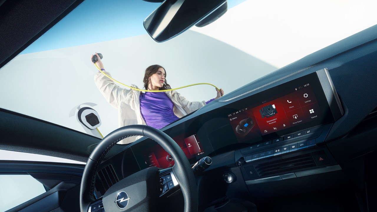 Gros plan de l'intérieur d'une Opel Astra Sports Tourer Electric avec, à l'extérieur, une femme tenant un câble de recharge pour véhicules électriques.