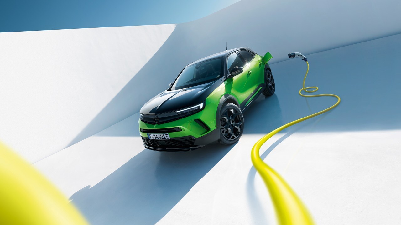 Vue latérale avant d'une Opel Mokka Electric verte avec des jantes noires et un toit avec un câble de recharge jaune.