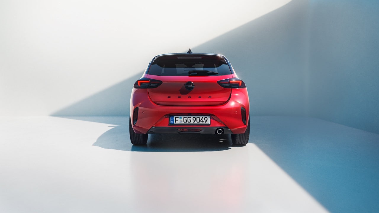 Femme debout à côté de la nouvelle Opel Corsa de couleur rouge avec toit noir et un homme qui monte par la porte du conducteur.